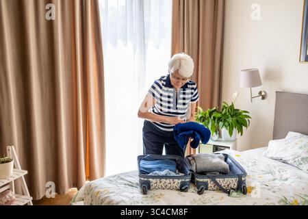 Eine ältere Frau, die einen Koffer für die Reise auf einem Bett zu Hause packt Stockfoto