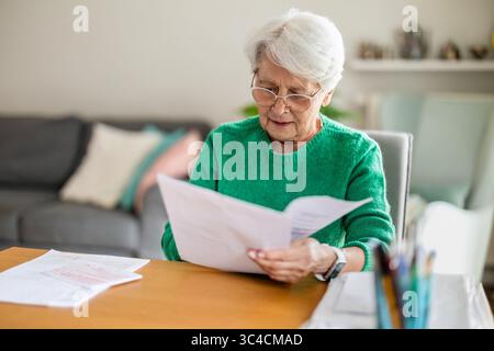 Eine ältere Frau sitzt im Wohnzimmer und macht Papierkram Stockfoto