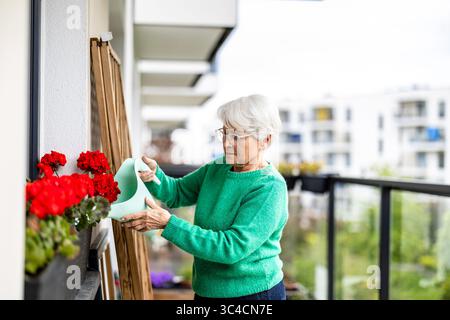 Ältere Frau, die Blumen auf dem Balkon ihres Hauses tränkt Stockfoto