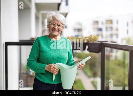 Ältere Frau, die Blumen auf dem Balkon ihres Hauses tränkt Stockfoto
