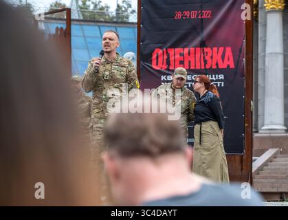 Kiew, Ukraine - 28. Juli 2025: Ukrainischer Soldat spricht während einer Gedenkfeier für die Opfer des Massakers im Gefängnis Oleniwka vor einem Banner, das das Datum des Angriffs zeigt. In der Nacht vom 28. Auf den 29. Juli 2022 beschossen die Russen die Gefängniskolonie Wolnovakha in der Nähe des besetzten Oleniwka. Mindestens 53 ukrainische Gefangene aus Asovstal wurden bei dem Terroranschlag getötet und mehr als 130 verletzt. Quelle: ARTEM HVOZDKOV/Alamy Live News Stockfoto