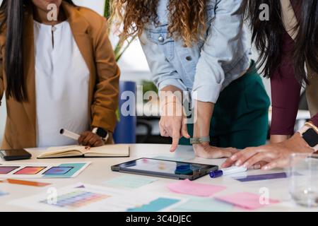 Verschiedene weibliche Kollegen arbeiten an digitalen Tablets und Farbausdrucken im Büro zusammen Stockfoto