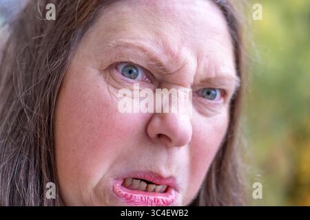 Gestresste 50-jährige Frau mit negativen Emotionen im Freien, umgeben von Grün und ruhiger Umgebung, reagiert mit Wut und Spannung, Emotionen Stockfoto