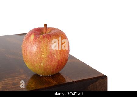 Frisches Wasser bestreut roten Apfel auf Eichenholz, isoliert auf weißem Hintergrund. Ernährungs- und Gesundheitskonzept. Stockfoto