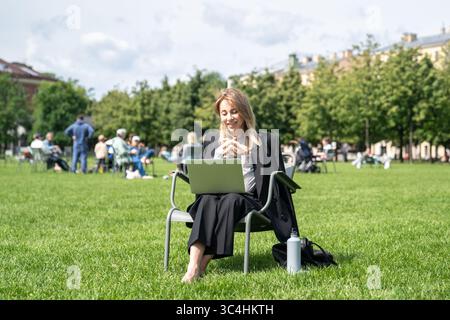 Freudige, reife Frau mit Laptop im Park, lächelnd auf den Bildschirm, am Wochenende Ausfallzeit Stockfoto