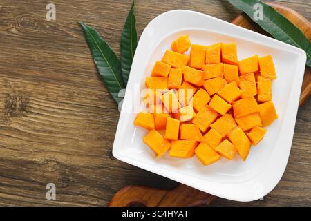 Ein Teller mit frisch geschnittenen Mangowürfeln, serviert auf einer weißen Schale auf einem Holztisch. Ein lebhafter tropischer Snack voller Geschmack und Farben. Stockfoto