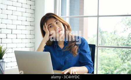Frau streckt den Arm hoch und sitzt falsch in der Position des Home Office-Schreibtisches. Rückseite einer jungen asiatischen Frau müde von der Arbeit Körper Stress Rücken Schmerz Büro Sy Stockfoto