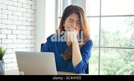 Frau streckt den Arm hoch und sitzt falsch in der Position des Home Office-Schreibtisches. Rückseite einer jungen asiatischen Frau müde von der Arbeit Körper Stress Rücken Schmerz Büro Sy Stockfoto