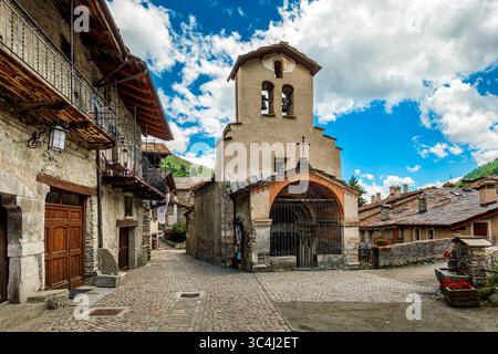Ein malerischer Blick auf die Kopfsteinpflasterstraße zwischen alten traditionellen Steinhäusern und mittelalterlicher Kirche in Chianale, Italien. Stockfoto