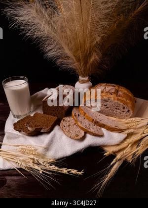 Rustikale Komposition aus frischem Brot, Milch und Weizenohren auf dunklem Hintergrund Stockfoto