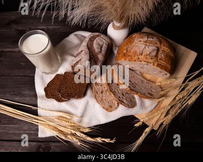 Ein gemütliches Stillleben-Arrangement mit verschiedenen Brotsorten auf einem Holzbrett, mit Scheiben dunklem Roggenbrot und einem Glas Milch Stockfoto
