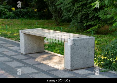 Eine Betonbank mit Holzsitz auf einem gepflasterten Parkweg, umgeben von üppigem Grün Stockfoto