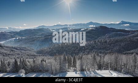 Helle Sonne, die über wunderschönen schneebedeckten Hügeln und Tälern der Karpaten strahlt, mit einem klaren blauen, sonnigen Himmel. Skigebiet Bukovel. Winter wilde Natur Reise Hintergrund Stockfoto
