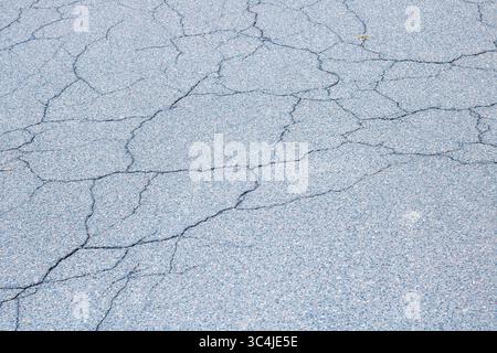Dies ist eine Nahaufnahme einer gerissenen Asphaltoberfläche, die ihre einzigartige Textur und ihr Muster wunderschön zeigt Stockfoto