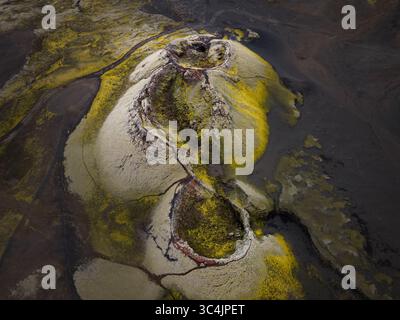 Aus der Vogelperspektive auf einen vulkanischen Krater, dessen Hänge mit lebhaftem Moos auf der krassen schwarzen Erde geschmückt sind, was eine surreale Landschaft erschafft, Island. Stockfoto
