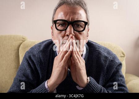 Nahaufnahme eines ernsten Mannes mittleren Alters mit Händen, die vor seinem Gesicht in einer Geste des Gebets oder der tiefen Besinnung gefesselt sind, und direkt auf das VI blickend Stockfoto