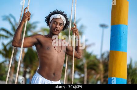 Fröhlicher, glücklicher schwarzer Mann mit Afro-Haaren, der an einem tropischen Strand lächelt und den Sommerurlaub genießt Stockfoto