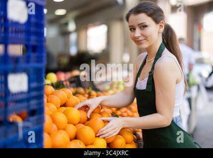 Arbeiten im Supermarkt - weibliche Verkäuferin sortiert reife Mandarinen auf der Vitrine Stockfoto