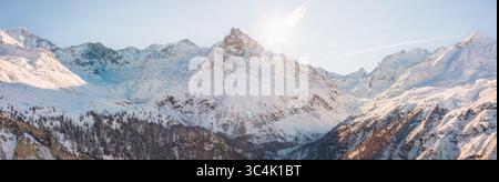 Aus der Vogelperspektive auf schneebedeckte Berge, die den Himmel durchdringen, während das strahlende Licht der Sonne lange Schatten über die unberührte Landschaft wirft, Zinal, Wallis, Schweiz. Stockfoto