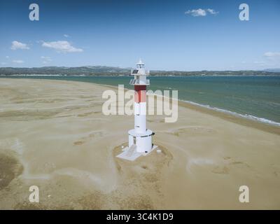Aus der Vogelperspektive auf den Leuchtturm Faro del Fangar, der hoch am Sandstrand steht, ein Leuchtfeuer vor dem ruhigen blauen Meer und Himmel, Deltebre, Katalonien, Spanien. Stockfoto