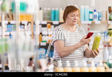 Seniorin in der Apotheke scannt QR-Code auf Haarausfall-Shampoo Stockfoto