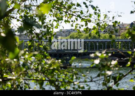 Eine Pariser Brücke, die teilweise von üppigem Grün verdeckt ist, schafft eine ruhige, idyllische Stimmung. Autos überqueren die Brücke und verleihen dem Stadtleben einen Hauch von Leben. Stockfoto