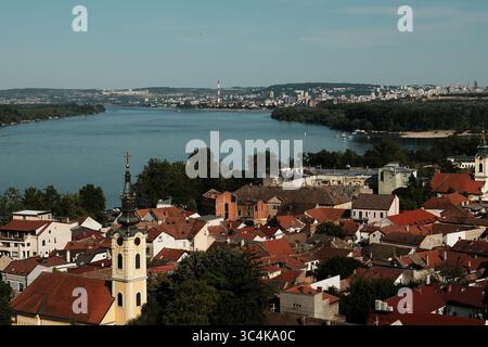 Großer Panoramablick auf Zemun mit Kirchen und roten Dächern entlang der Donau, Belgrad ist in der Ferne über den Fluss sichtbar. Stockfoto