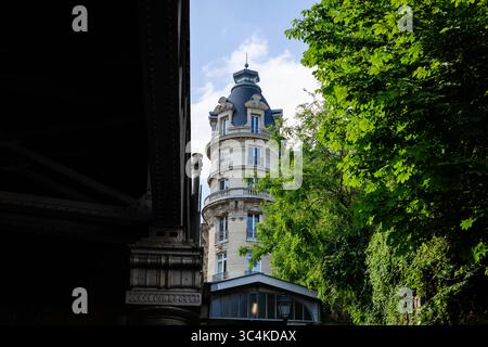 Die elegante Kuppel und die verzierte Fassade eines Pariser Gebäudes blicken durch üppiges Grün und schaffen eine ruhige, raffinierte Atmosphäre. Die dunkle Metallstruktur Stockfoto