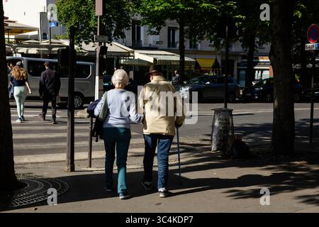 Ein älteres Paar schlendert Hand in Hand eine Pariser Straße hinunter, im Sonnenlicht getaucht. Ihre Rückansicht betont Intimität und friedliches Altern. Ideal für Stockfoto