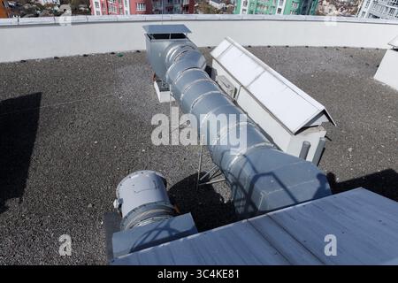 Blick aus der Vogelperspektive auf das Dach mit großem Lüftungssystem und Kiesfläche in urbaner Umgebung in der Nähe von Wohngebäuden unter klarem blauem Himmel Stockfoto