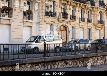 Eine Pariser Straßenszene: Drei Fahrzeuge parkten vor einem klassischen Haussmann-Gebäude. Verzierte Eisenbalkone und eine Holztür betonen die des Gebäudes Stockfoto