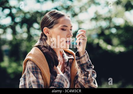 Junge Frau im Freien mit Inhalator während einer AsthmaEpisode an einem hellen sonnigen Tag in einem grünen Park Stockfoto