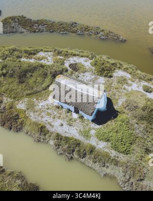 Aus der Vogelperspektive eines einsamen Hauses mit einem Strohdach, inmitten der ruhigen Wasserstraßen und grünen Inseln des Deltas, Delta del Ebro, Katalonien, Spanien. Stockfoto