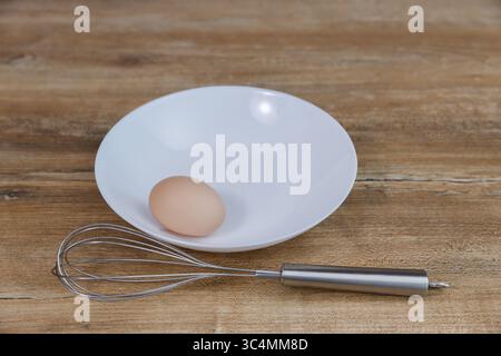 Ein einfaches kulinarisches Setup: Ein Ei und ein Schneebesen auf einem Teller, bereit zum Kochen oder Backen in einer sauberen Küchenumgebung Stockfoto