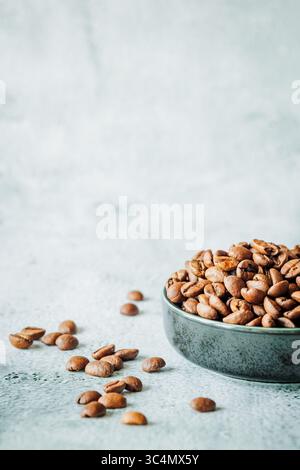 Schüssel mit gerösteten Kaffeebohnen und ein paar Bohnen auf einer strukturierten Betonoberfläche gegen luftigen Negativraum, minimal und rustikal Stockfoto