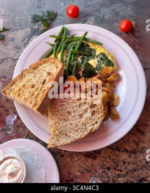 Frühstück mit Toast, Omelett mit Spinat und Bohnen und gebratenen Kartoffeln auf einem weißen Teller. Draufsicht Stockfoto