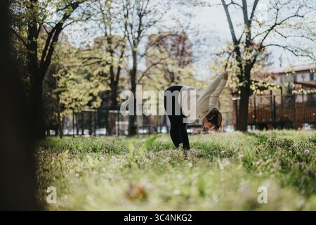 Junge Frau, die draußen in einem sonnigen Park mit Bäumen trainiert Stockfoto