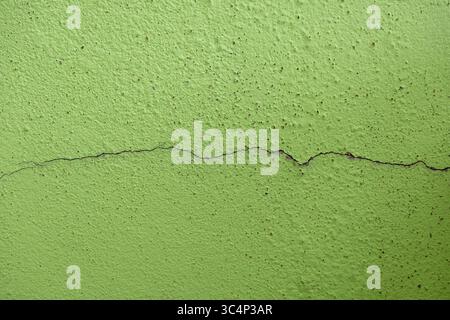 Verwitterte Gebäudewand mit dünnen Rissen. Dunkle Punktlöcher sind auf der grün lackierten Oberfläche gut sichtbar. Zeigt Verfall, Beschädigung und urbane Textur. Ideal für Stockfoto