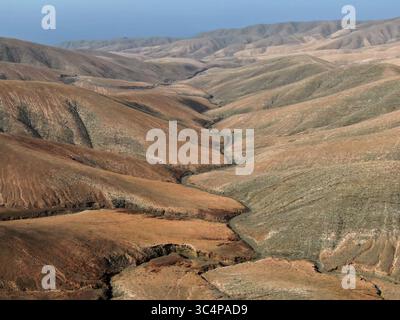 Aus der Vogelperspektive schroffe, hügelige Hügel mit kontrastierenden Erdtönen und tiefen Schatten schaffen eine faszinierende Landschaft, Fuerteventura, die Kanarischen Inseln, Spanien. Stockfoto