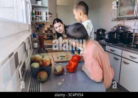 Kinder bereiten Gemüse zusammen in einer hellen Küche zu, schneiden Gurken und genießen die Zeit der Familie. Lernen, Teilen und gesunde Ernährung in A Stockfoto