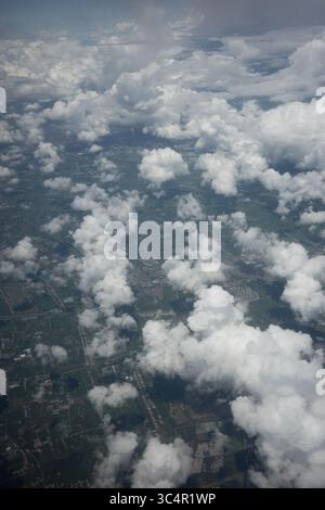 Aus der Vogelperspektive sehen Sie ein atemberaubendes Mosaik aus weißen Cumulus-Wolken, die über einer vielfältigen Landschaft aus grünen Feldern und verstreuten Wohngebieten schweben. Stockfoto