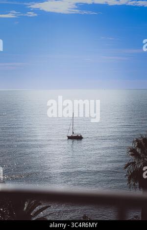 Blick auf den Sonnenuntergang vom Fenster des Mittelmeers aus ist eine vorbeisegelnde Yacht am Horizont sichtbar. Das Foto wurde in Südfrankreich aufgenommen. Stockfoto
