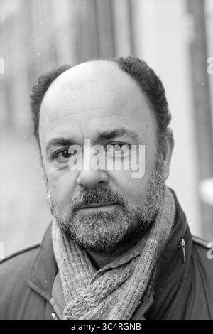 Herr Sevil, Gemeindeentwickler Frans Halsbuurt, Ausländer, Viertel, Gemeindezentren, örtliche Geschäfte, Trainingszentren, 24-11-1983 Whizgle News, Dutch Desk, Niederlande, 1950-2000 Ein Mann mit einem durchdachten Ausdruck, der einen gut gepflegten Bart und einen hervorragenden Glatzkopf zeigt, trägt einen Schal und einen Mantel. Sein Blick deutet auf Nachsicht hin, während er vor einem sanft verschwommenen Hintergrund steht. Stockfoto