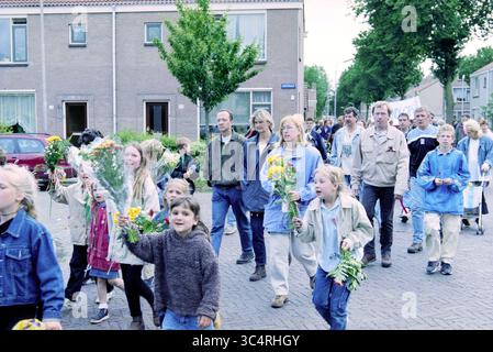 Ankunft der viertägigen Abendveranstaltung, IJmuiden, IJmuiden, Niederlande, 09-06-1999 Whizgle News, Dutch Desk, Niederlande, 1950-2000 Eine vielfältige Gruppe von Menschen, darunter Kinder und Erwachsene, marschieren gemeinsam eine Straße hinunter und halten Blumensträuße. Die Atmosphäre ist lebendig und gemeinschaftsorientiert, mit Einzelpersonen in lässiger Kleidung, einige lächeln und interagieren miteinander, während sie an einer gemeinsamen Veranstaltung teilnehmen. Stockfoto
