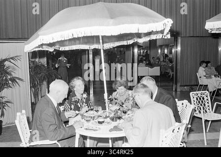 50. Jahrestag der CBR, Partymitarbeiter, C.B.R., 08-10-1977 Whizgle News, Dutch Desk, Niederlande, 1950-2000 Eine Gruppe elegant gekleideter Einzelpersonen genießt eine gemeinsame Mahlzeit unter einem großen Sonnenschirm, umgeben von einem stilvollen Speisesaal. Die Atmosphäre ist lebhaft, mit zusätzlichen Gästen im Hintergrund, die sich mit Gesprächen und Speisen beschäftigen. Stockfoto