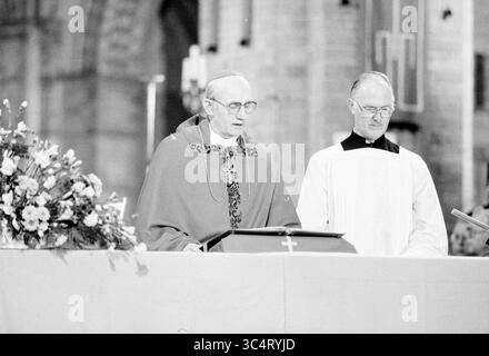 Bischof Bomers und Weihbischof Lescrauwaert, RK Bavo, Haarlem, Weihe, römisch-katholische Kirche, Haarlem, Niederlande, 14-01-1984 Whizgle News, Dutch Desk, Niederlande, 1950-2000 Ein Klerus hält eine Predigt bei einer religiösen Zeremonie, begleitet von einem anderen Kleriker. Das Ambiente ist mit Blumenarrangements und religiösen Symbolen versehen, die eine feierliche Atmosphäre schaffen. Stockfoto