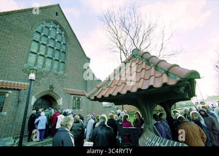 Fahrt zur Kirche, IJmuiden, IJmuiden, Niederlande, 01-04-2003 Whizgle News, Dutch Desk, Niederlande, 1950-2000 Eine große Menschenmenge versammelt sich vor einem historischen Backsteingebäude mit komplizierter Architektur, die eifrig in der Nähe eines traditionellen Brunnens mit einem gekachelten Dach warten. Die Szene fängt ein Gefühl von Gemeinschaft und Vorfreude ein. Stockfoto
