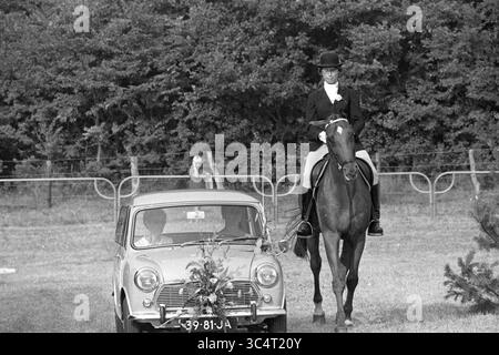 A. Ebben, Gewinner MB, Wettbewerb, 02.08.1969 Whizgle News, Dutch Desk, Niederlande, 1950-2000 Ein Reiter in formeller Kleidung sitzt anmutig auf einem Pferd, während ein Oldtimer mit Blumenschmuck in der Nähe parkt. Die Szene spielt in einem üppigen, grünen Feld, umgeben von Bäumen und einem fernen Zuschauer. Stockfoto