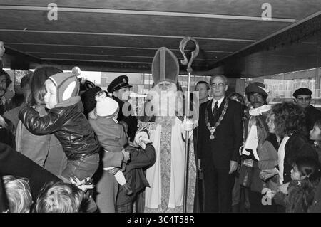 St. Nikolaus in IJmuiden - Heemskerk - Velsen-Noord, St. Nikolaus, Sinterklaas, 23-11-1974 Whizgle News, Dutch Desk, Niederlande, 1950-2000 Eine große Gruppe von Menschen, darunter Kinder, versammelt sich um eine Figur, die in aufwendigen Gewändern und einem hohen, spitzen Hut gekleidet ist. Die Figur, die einem traditionellen heiligen ähnelt, hält einen Stab und ist von verschiedenen Zuschauern umgeben, darunter Beamte in Anzügen und Familien. Die Atmosphäre ist festlich und neugierig. Die Kinder greifen nach außen, um sich mit der zentralen Figur zu beschäftigen. Stockfoto