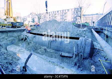 Entsorgung des alten Öltanks von der Hochschule Amsterdam, Amsterdam, Niederlande, 14-12-1999 Whizgle News, Dutch Desk, Niederlande, 1950-2000 Eine Baustelle mit Arbeitern in Sicherheitsausrüstung, die eine große, zylindrische Struktur, umgeben von ausgegrabener Erde und Maschinen, ausheben. Wasser sammelt sich im Graben, was auf die kürzliche Grabtätigkeit hinweist. Stockfoto
